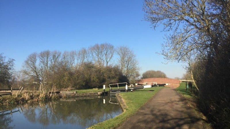 A canal towpath beside a lock and still water under a clear blue winter sky
